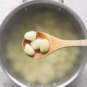 A wooden spoon holds several pieces of gnocchi over a pot of boiling water.