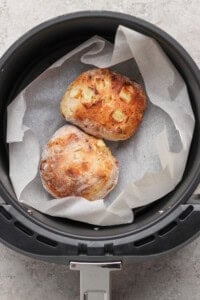 Two small round loaves of bread with a rustic crust rest on parchment paper inside an air fryer basket.