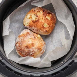 Two small round loaves of bread with a rustic crust rest on parchment paper inside an air fryer basket.