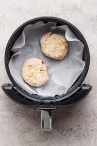 Two unbaked dough rounds with visible chunks, placed on parchment paper inside an air fryer basket.