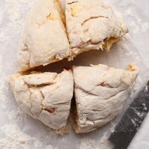 Round ball of uncooked dough cut into four equal pieces on floured parchment paper, with a knife placed beside it.