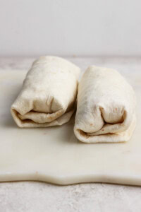 Two neatly wrapped burritos placed side by side on a white cutting board.