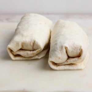 Two neatly wrapped burritos placed side by side on a white cutting board.