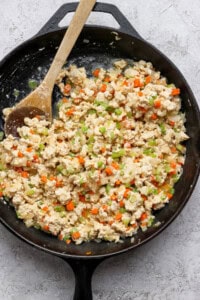 A cast iron skillet filled with scrambled tofu mixed with diced carrots, celery, onions, and a wooden spoon on the side.