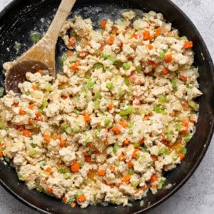 A cast iron skillet filled with scrambled tofu mixed with diced carrots, celery, onions, and a wooden spoon on the side.
