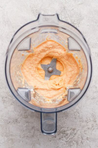 A blender with creamy, light orange mixture spread around the blades, viewed from above on a textured surface.