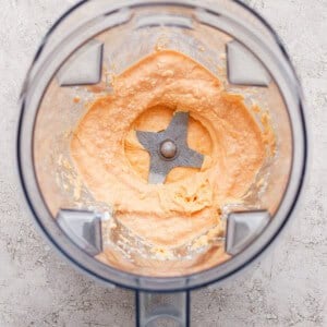 A blender with creamy, light orange mixture spread around the blades, viewed from above on a textured surface.
