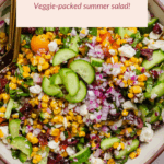 A bowl of Mediterranean corn salad with chopped cucumber, red onion, cherry tomatoes, corn, feta, and olives, with a serving spoon. Text overlay reads "Mediterranean Corn Salad.
