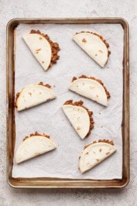 Six folded flour tortillas filled with ground beef are arranged on a parchment-lined baking sheet.