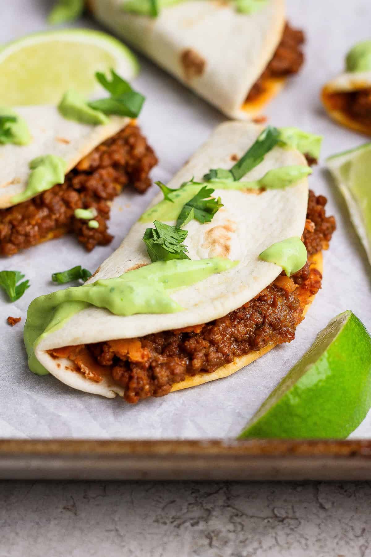 A taco filled with seasoned ground meat, topped with green sauce and cilantro, served on a tray with lime wedges.