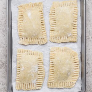 Four unbaked rectangular hand pies with crimped edges are arranged on a parchment-lined baking sheet.