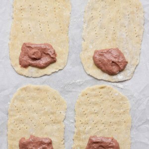 Four rectangular dough pieces, each with fork marks and a portion of meat paste on one end, are arranged on a parchment-lined surface.