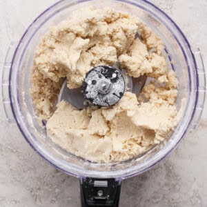 A food processor filled with partially mixed dough sits on a light-colored countertop.