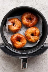 Four golden brown bagels on parchment paper inside an air fryer basket.