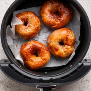 Four golden brown bagels on parchment paper inside an air fryer basket.