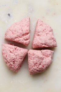 Four pieces of pinkish dough are arranged on a white, lightly floured surface.