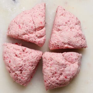 Four pieces of pinkish dough are arranged on a white, lightly floured surface.