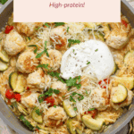 A skillet filled with orzo pasta, chicken meatballs, zucchini, cherry tomatoes, parmesan cheese, and a dollop of yogurt, garnished with chopped herbs.