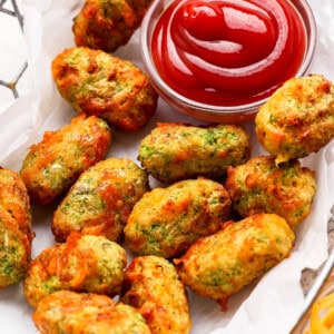 A basket of baked vegetable tots served with a small bowl of ketchup for dipping.