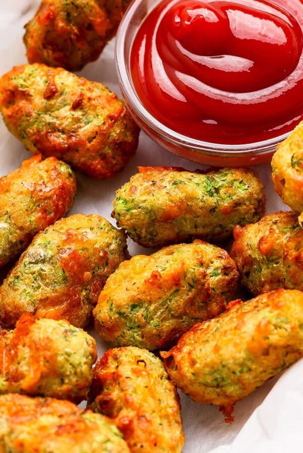A basket of baked vegetable tots served with a small bowl of ketchup for dipping.