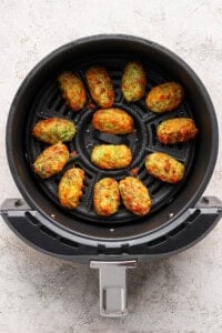 Twelve cooked vegetable tots arranged in a single layer inside the basket of an air fryer.