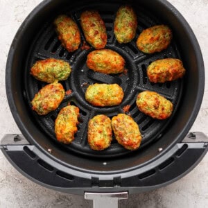 Twelve cooked vegetable tots arranged in a single layer inside the basket of an air fryer.
