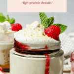 A glass jar filled with cottage cheese cheesecake, topped with whipped cream, a raspberry, mint leaves, and a drizzle of red sauce, labeled as a high-protein dessert.