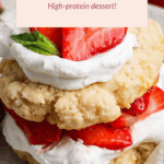 A cottage cheese strawberry shortcake topped with whipped cream, fresh strawberries, and a mint leaf on a white plate. Text overlay promotes it as a high-protein dessert.