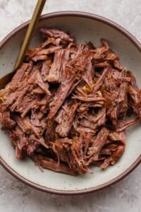 A bowl filled with shredded cooked beef, with a fork resting on the side.