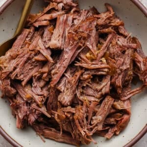 A bowl filled with shredded cooked beef, with a fork resting on the side.