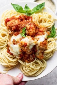 A plate of spaghetti topped with meatballs, tomato sauce, melted cheese, and garnished with fresh basil leaves.