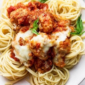 A plate of spaghetti topped with meatballs, tomato sauce, melted cheese, and garnished with fresh basil leaves.