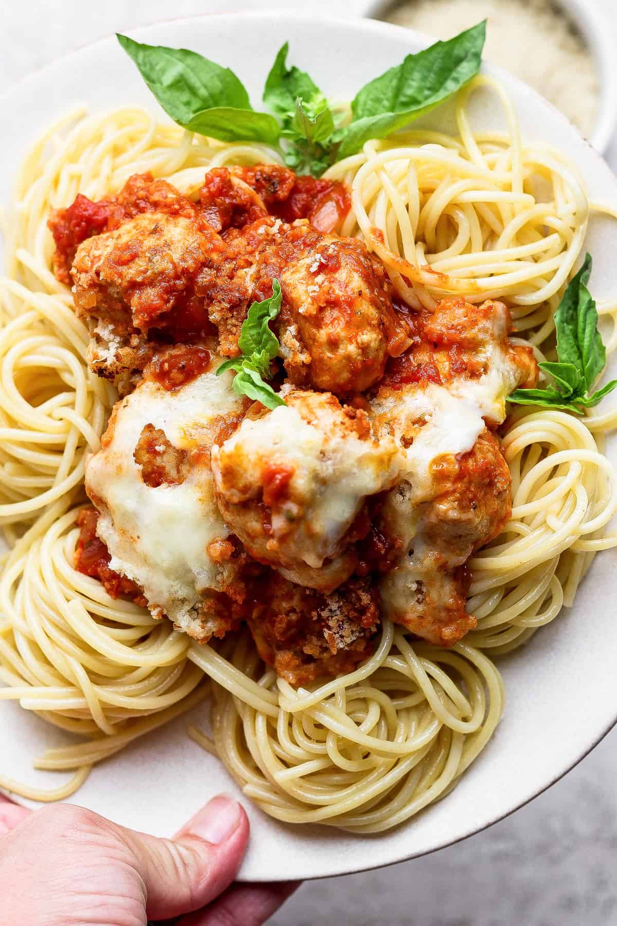 A plate of spaghetti topped with meatballs, tomato sauce, melted cheese, and garnished with fresh basil leaves.