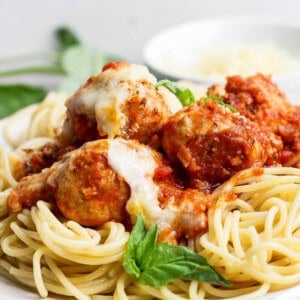 A plate of spaghetti topped with tomato sauce, meatballs, melted cheese, and a fresh basil garnish.
