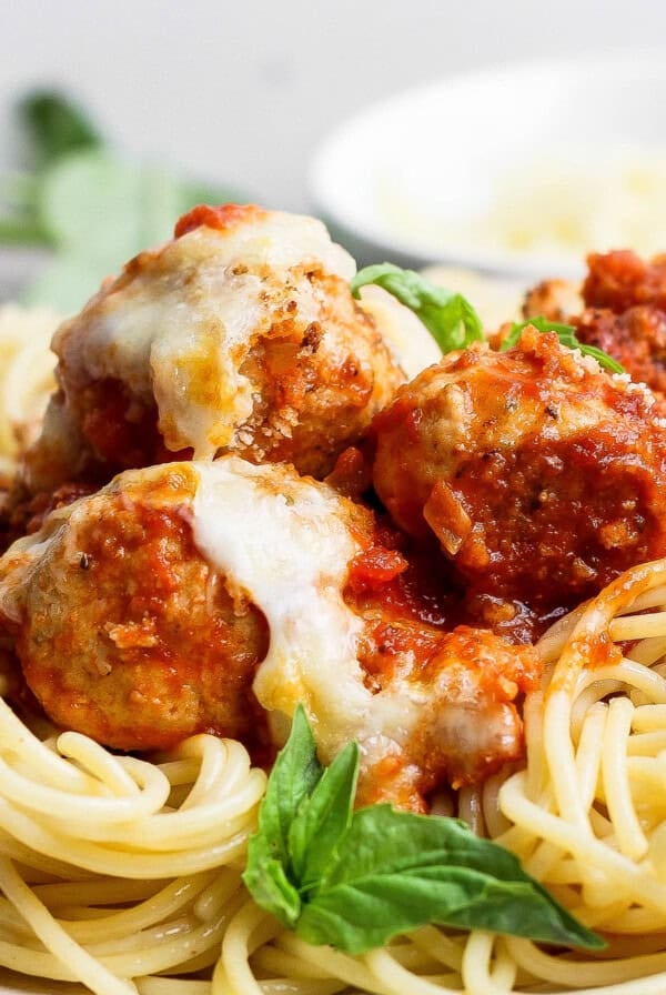 A plate of spaghetti topped with tomato sauce, meatballs, melted cheese, and a fresh basil garnish.