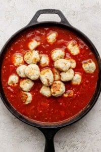 A cast iron skillet filled with meatballs in tomato sauce on a light textured surface.