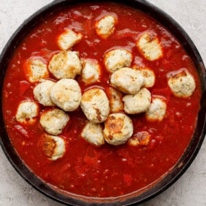 A cast iron skillet filled with meatballs in tomato sauce on a light textured surface.