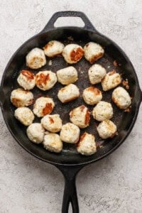 Cooked meatballs are arranged in a black cast iron skillet on a light textured surface.