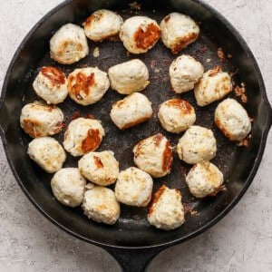 Cooked meatballs are arranged in a black cast iron skillet on a light textured surface.