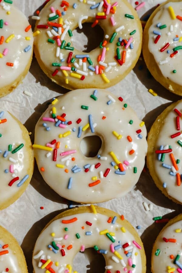 Glazed donuts topped with colorful sprinkles are arranged closely together on a light surface.