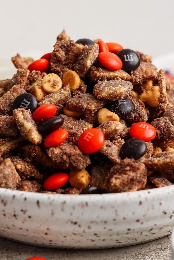 A bowl filled with chocolate-coated nuts or snack mix, topped with orange and brown M&M’s and butterscotch chips.