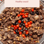 A bowl of pumpkin protein puppy chow snack mix topped with orange and brown candies, with a label reading "Pumpkin Protein Puppy Chow Healthy snack!.