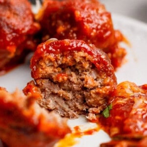 A close-up of a partially eaten meatball covered in tomato sauce, revealing its cooked, ground meat interior.