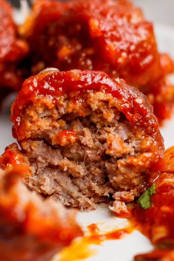A close-up of a partially eaten meatball covered in tomato sauce, revealing its cooked, ground meat interior.