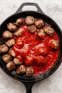 A cast iron skillet filled with meatballs arranged around a pool of tomato sauce on a light textured surface.