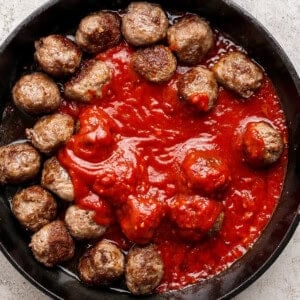 A cast iron skillet filled with meatballs arranged around a pool of tomato sauce on a light textured surface.