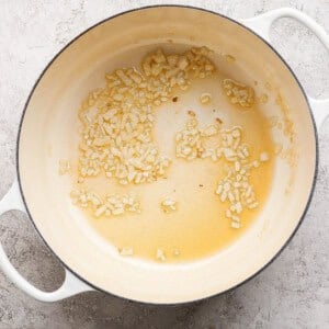 Chopped onions sautéing in oil in a large white pot on a light-colored surface.