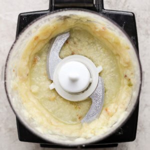 Top view of a food processor containing a pale, creamy blended mixture with visible metal blades in the center.