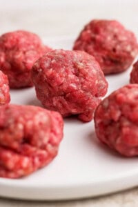 Several raw ground beef meatballs arranged on a white plate.