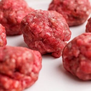 Several raw ground beef meatballs arranged on a white plate.